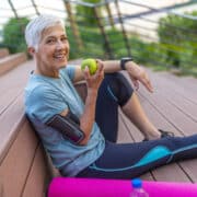 Sportos nő almát eszik. Ősz hajú nő a hatvanas évei elején sportedzés után pihen.