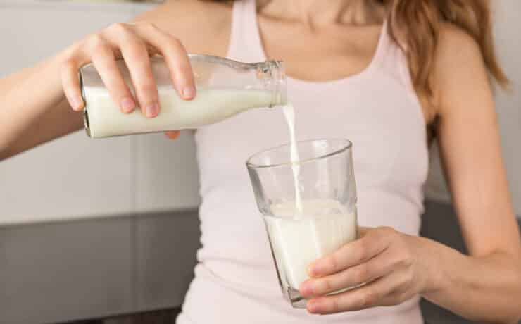 Egy nő tejet önt az üvegből a pohárba.