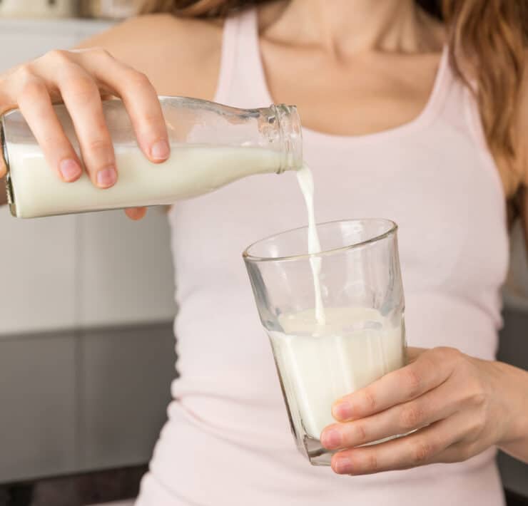 Egy nő tejet önt az üvegből a pohárba.