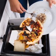 Közeli fotó egy kukába dobott pizzáról, ami az ételpazarlás illusztrációja