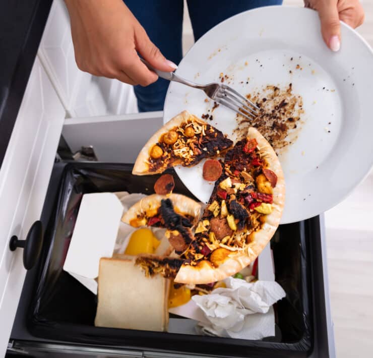 Közeli fotó egy kukába dobott pizzáról, ami az ételpazarlás illusztrációja