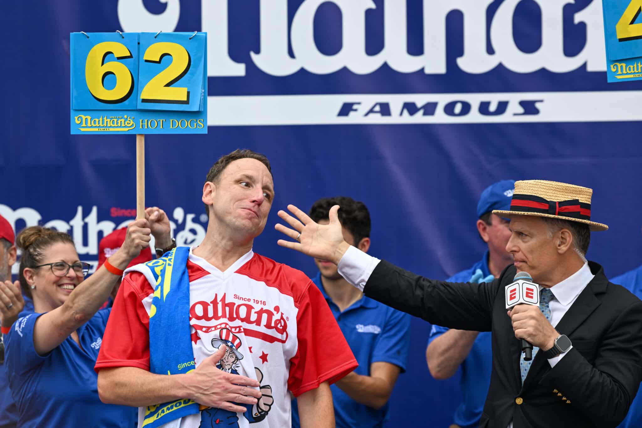 Joey Chestnut amerikai versenyevő áll baloldalt a verseny színhelyén, jobboldalt a műsorvezető