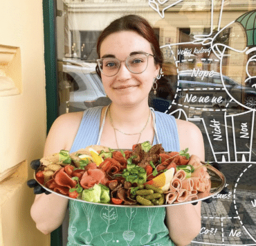Egy prágai vegán hentes üzlet dolgozója tart maga előtt egy hidegtálat, amin növényi alapú sonkatekercsek, tojás és zöldségek vannak