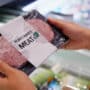 Két kéz tart egy vegán húshelyettesítő terméket, amin a "Plant-based meat" felirat olvasható