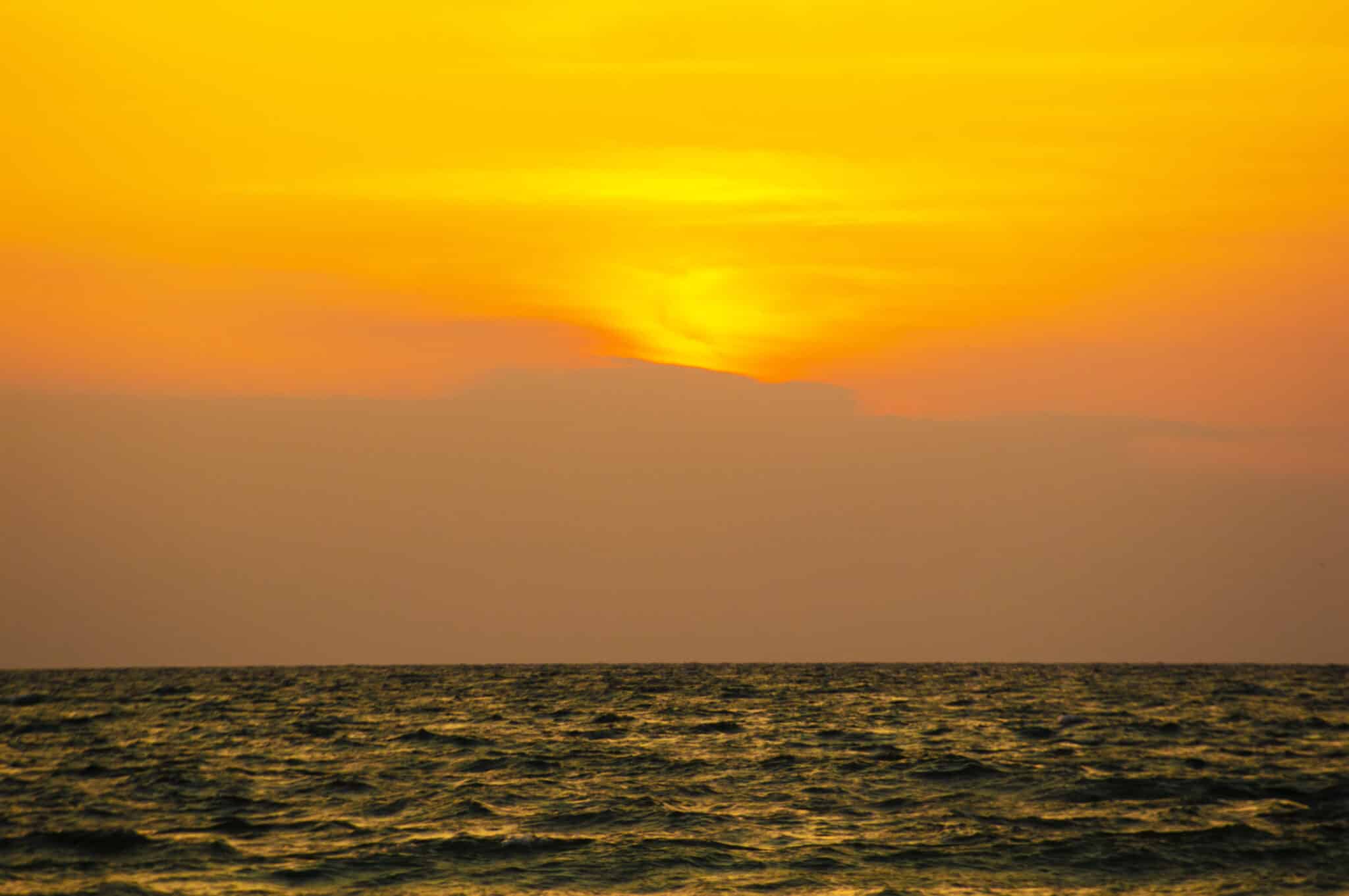 Elöl a tenger, amit kissé megvilágít a háttérben a hegyek mögött épp lebukó nap