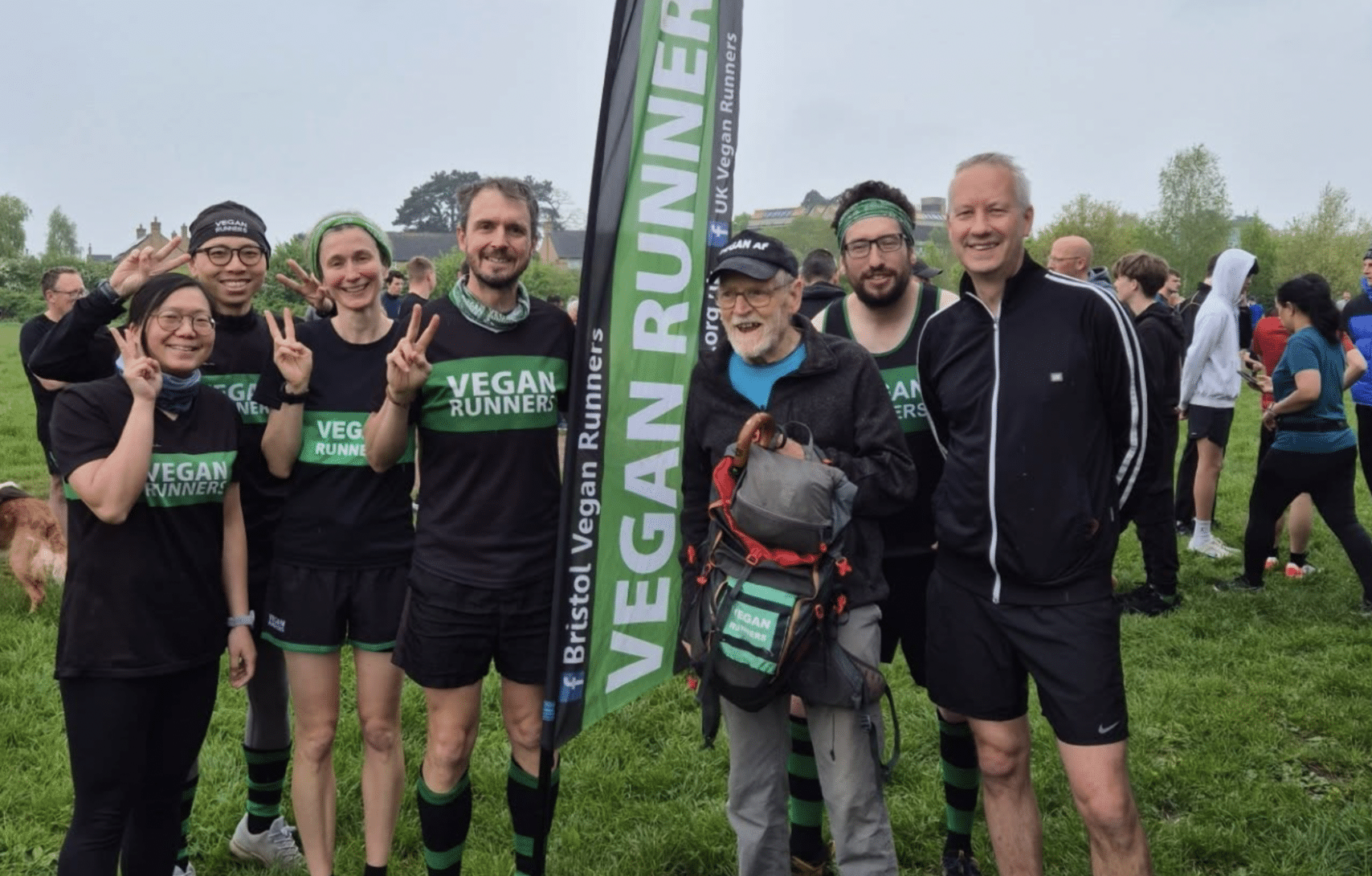 Paul Youd 87 éves vegán ultramaratonista és több másik futó pózolnak és mosolyognak a kamerába nézve egy "Vegan runners" feliratú zászló mellett