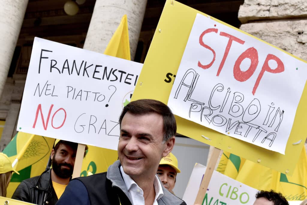 A hús- és tejipar képviselői táblákkal tiltakoznak a szintetikus hús ellen Olaszországban. A kép előreterében Ettore Prandini, a Coldiretti termelői szövetség elnöke mosolyog.