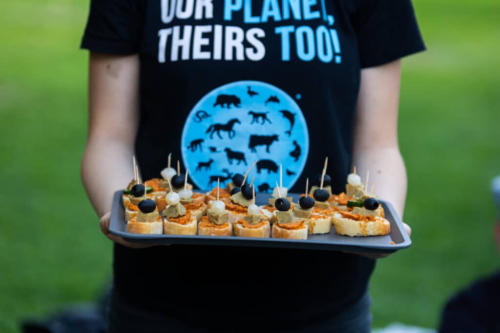 Mini szendvicsekkel megrakott tálcát tart valaki, akinek a pólóján a következő szöveg olvasható: Our Planet. Theirs too!