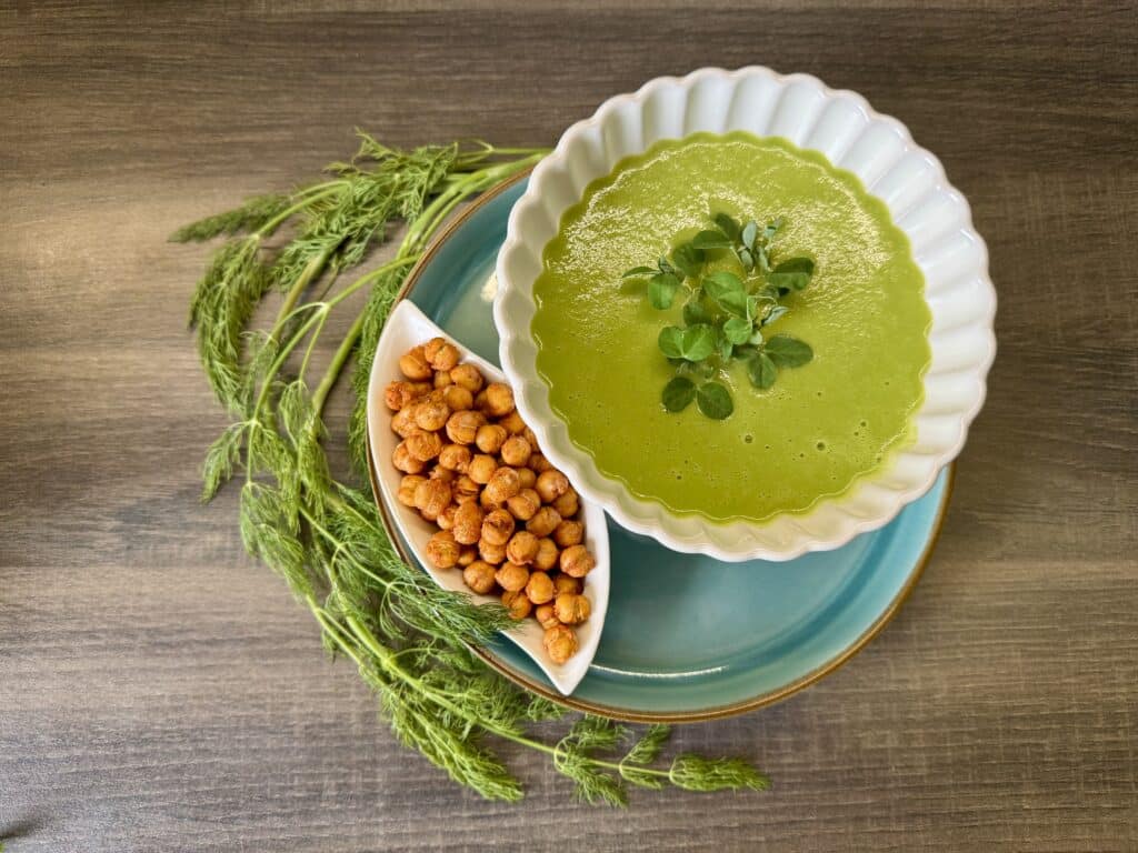 Kovászosuborka-leves fehér mélytányérban, mellette sült csicseriborsó és díszítésnek egy szál kapor