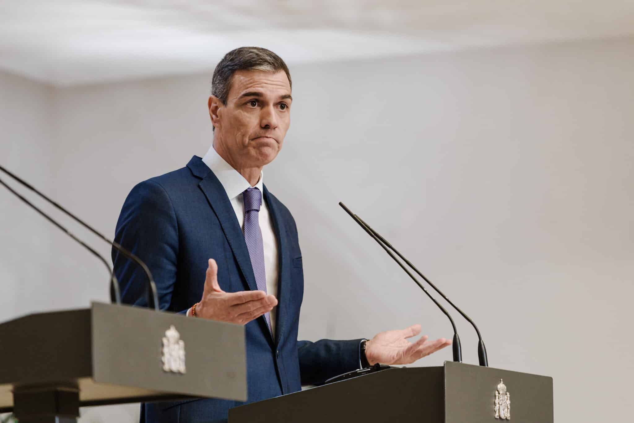 Pedro Sánchez spanyol kormányfő pulpitusnál állva beszédet mond. Karjait széttárja, szája lefelé görbül