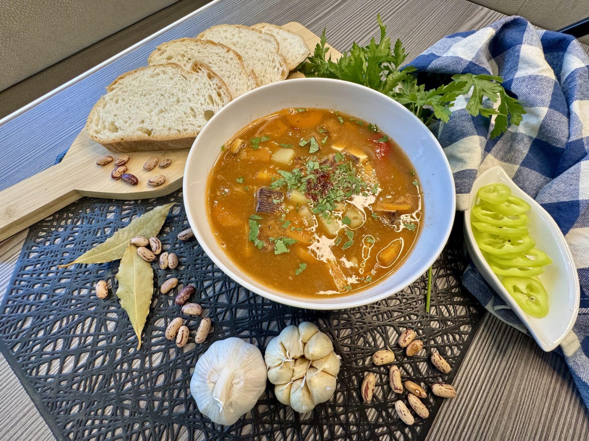 Jókai bableves tányérban, mellett kenyérszeletek, babérlevél, fokhagyma, petrezselyem és zöld paprika