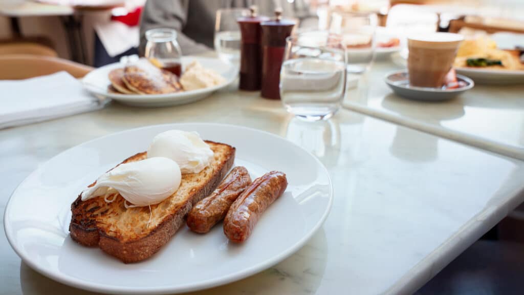 Asztalon tányér, rajta pirítós tojással, kolbásszal.