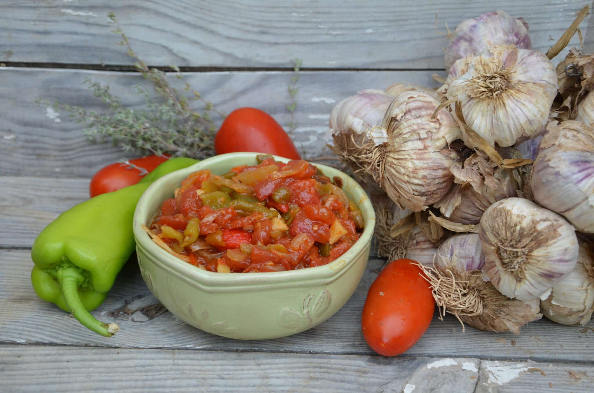 Piperade, baszk zöldségragu egy zöld tányérban, körülötte paradicsom, paprika és hagyma