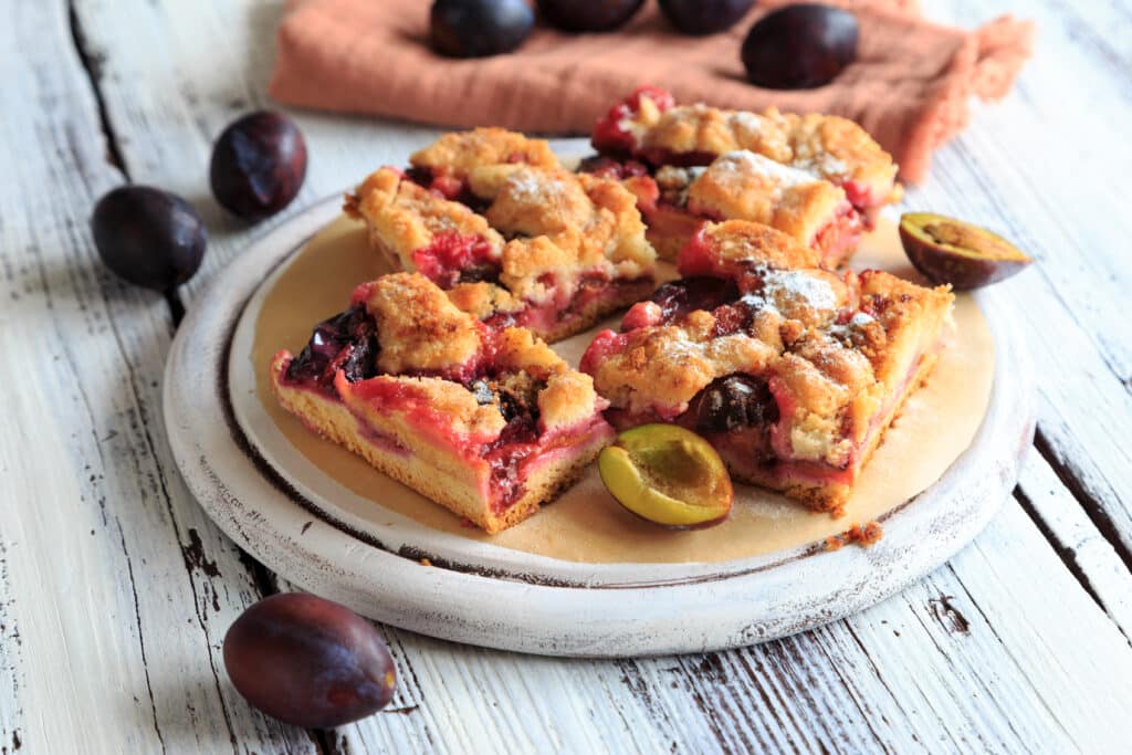 Szilvás morzsasüti felszeletelve, mellette egész és felezett szilvák