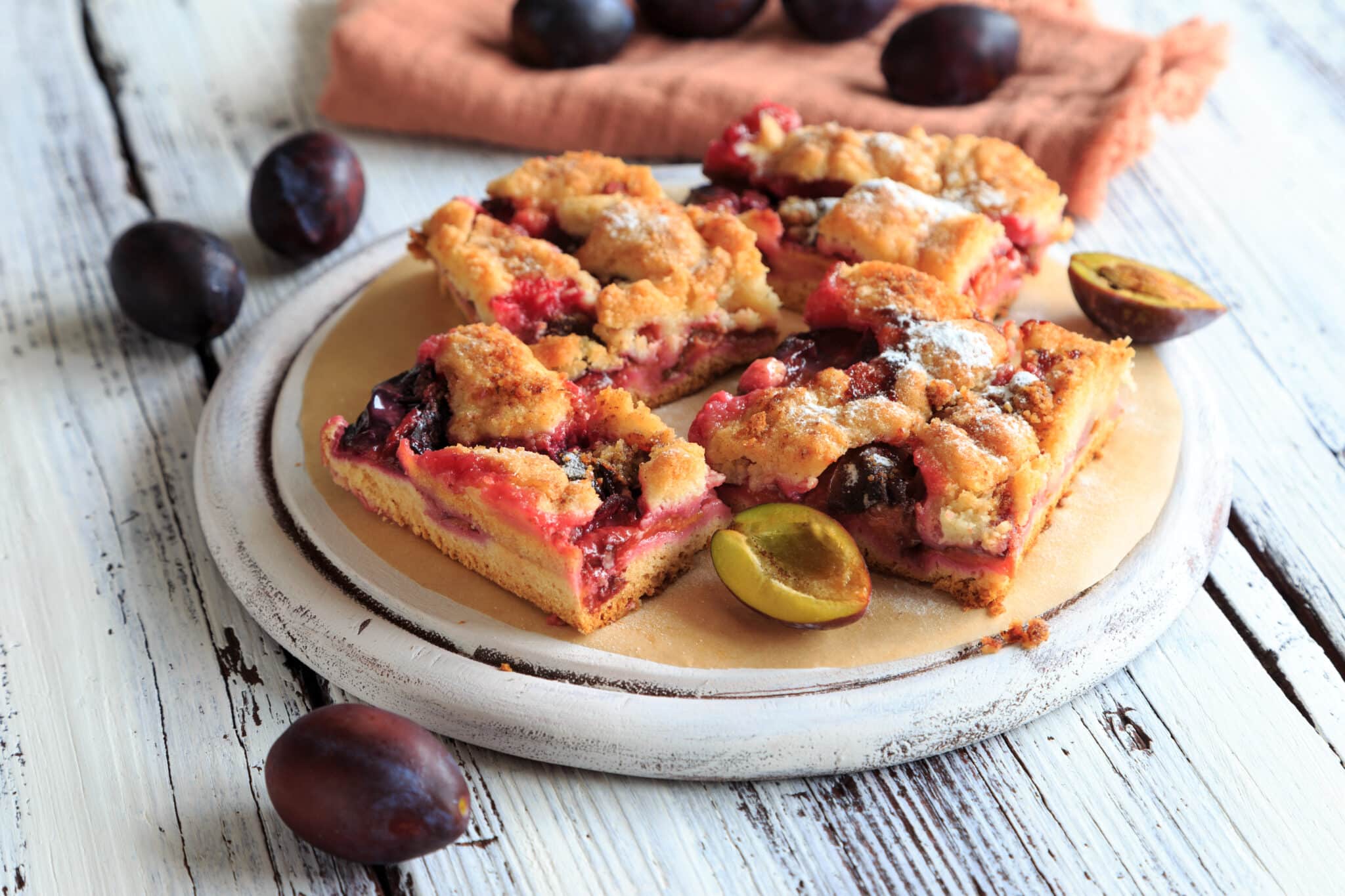 Szilvás morzsasüti felszeletelve, mellette egész és felezett szilvák