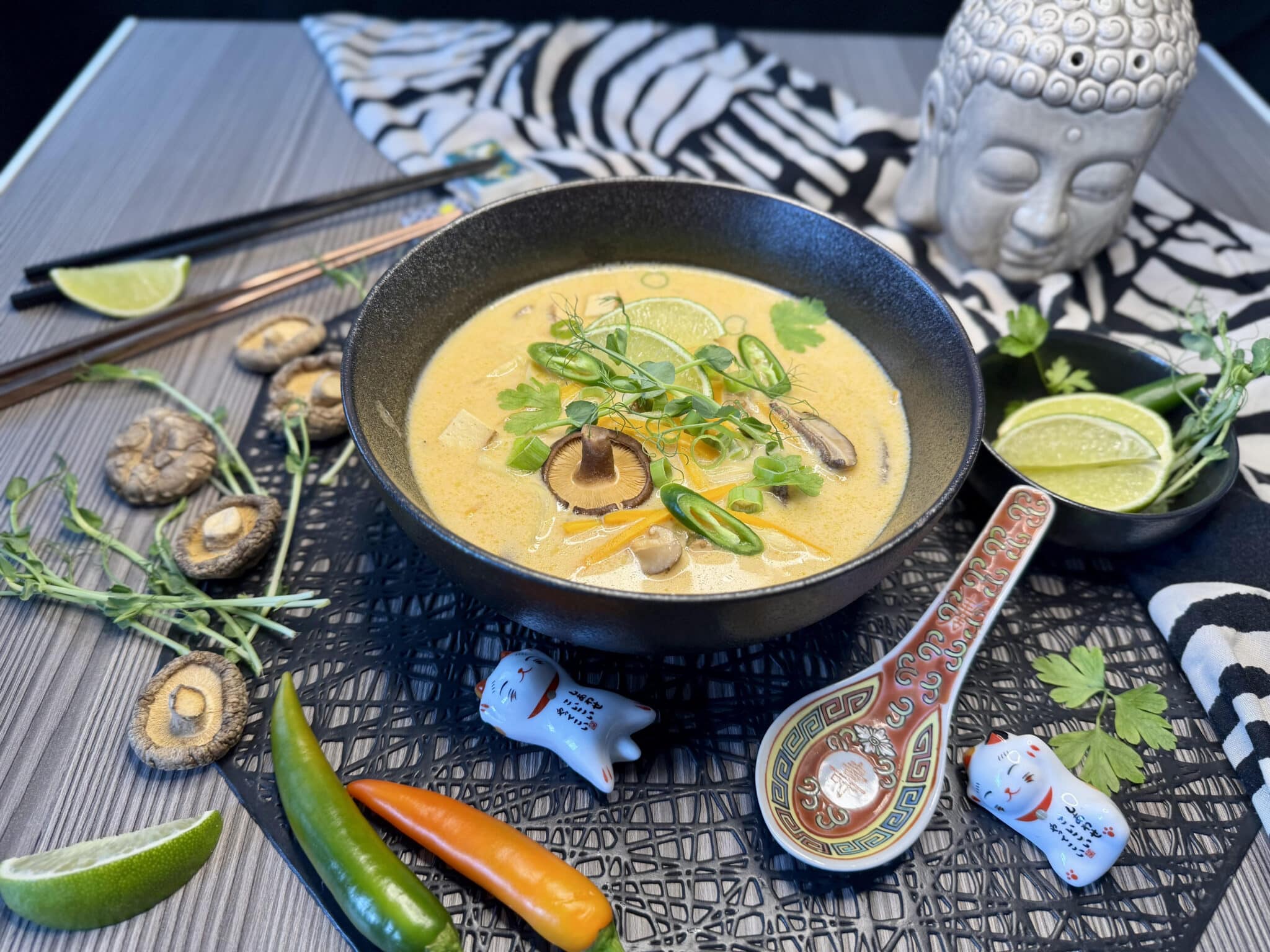 Vegán Tom Kha leves fekete tányérban, mellette ázsiai asztaldíszekkel