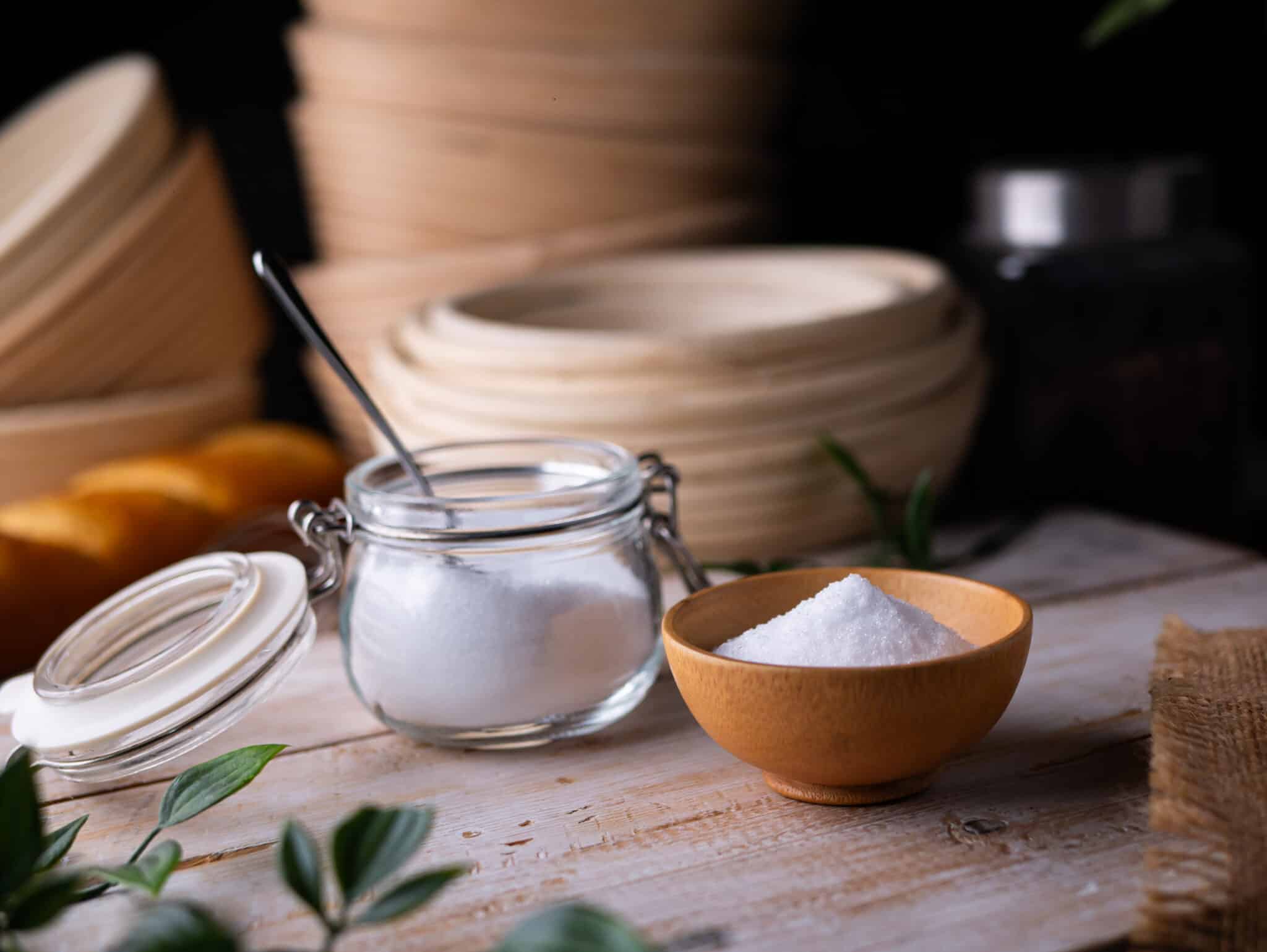 Eritrit áttetsző csatos üvegben, benne kiskanál, mellette egy barna edénykében is eritrit látható