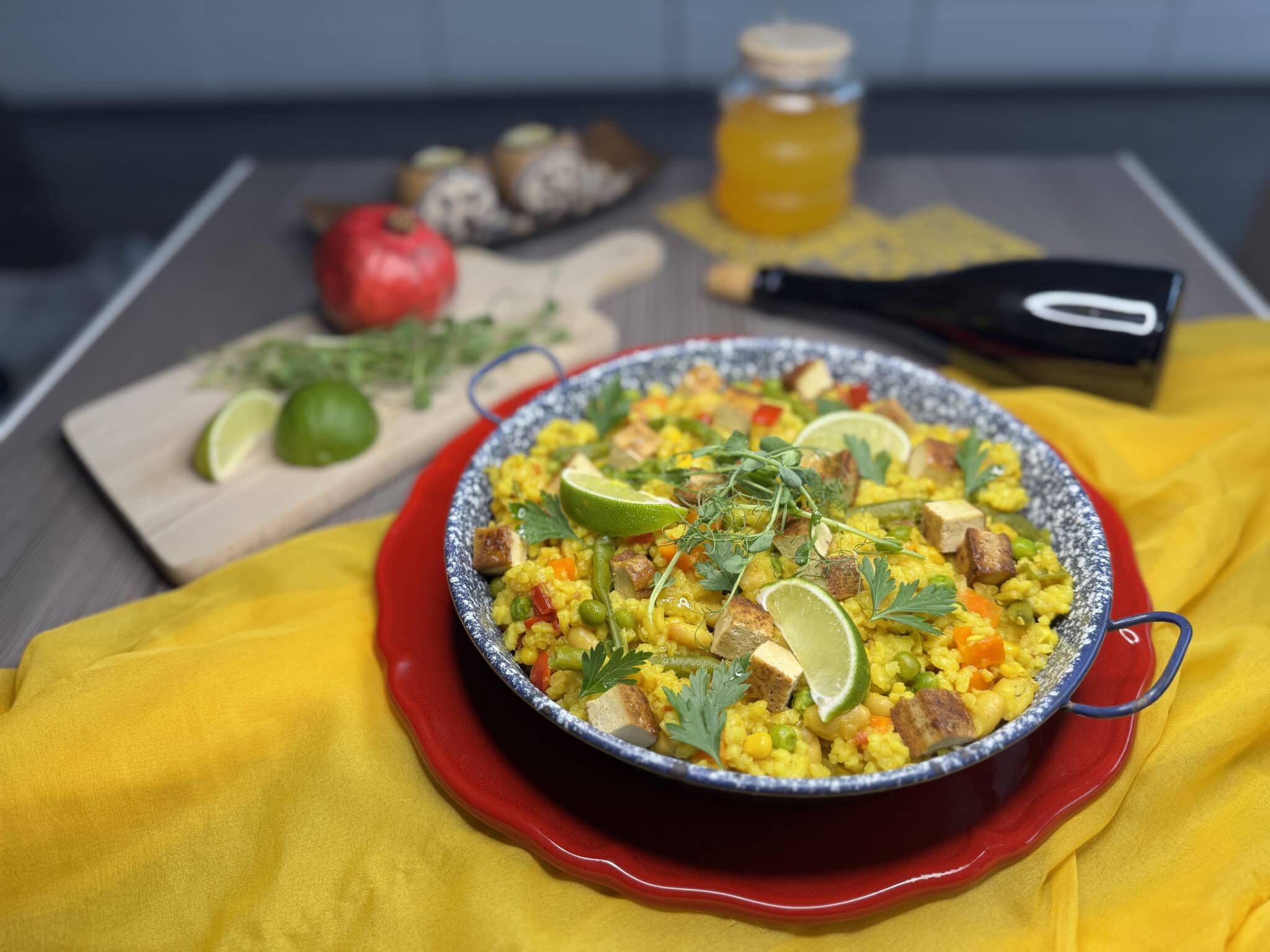 Egy tál színes paella, rajta pár gerezd lime, a háttérben zöldségek