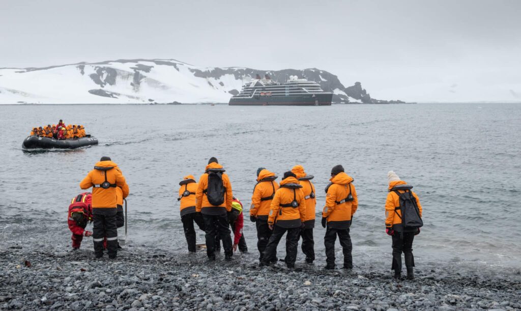 Tudósok és turisták narancssárga kabátban az Antarktiszi-félszigeten